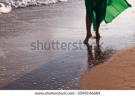 Beautiful woman in green dress walking barefoot on the beach.