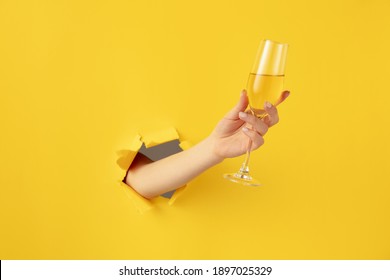 Beautiful Woman Hand With Champagne Flute Breaks Through Yellow Background