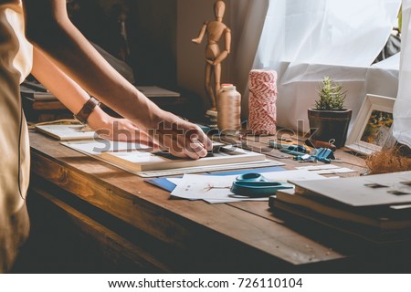 Beautiful woman hand crafting book at the tabletop with stationery. Stylish craftswoman with stationery work at his hipster workstation.