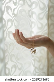 Beautiful woman hand holding a luxury gold necklace with a world map locket against a white sheer curtain