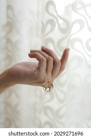 Beautiful woman hand holding a luxury gold necklace with a world map locket against a white sheer curtain