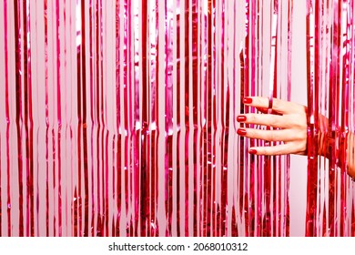 Beautiful Woman Hand With Nail Polish In Red Breaking Through A Pink Tinsel. Ready For Special Party.