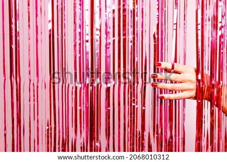 Beautiful woman hand with nail polish in red breaking through a pink tinsel. Ready for special party.