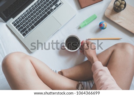 Beautiful woman hands holding cups of coffee and using laptop on the bed in the house.