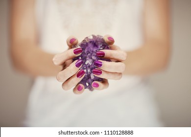 Beautiful woman hands with perfect pink nail polish holding violet amethyst crystal, can be used as background
