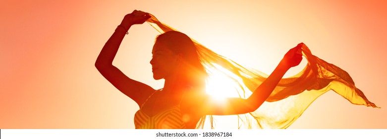 Beautiful woman happy free in summer sunset glow waving scarf in the wind dancing in sun panoramic banner. Silhouette feminine lady freedom for wellness and healthy living.