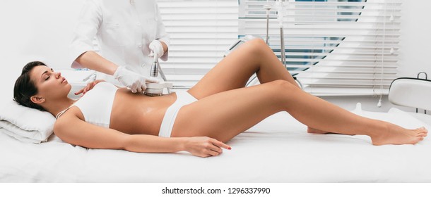 Beautiful woman having cavitation, procedure removing cellulite on her abdomen at beauty clinic