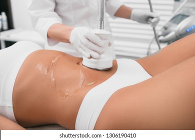 Beautiful woman having cavitation, procedure removing cellulite on her belly at beauty clinic