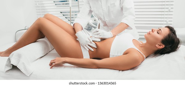 Beautiful woman having cavitation, procedure removing cellulite on her abdomen at beauty clinic