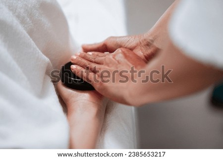 Beautiful woman having hot stones on her back in spa salon. concept of healthcare and female beauty. masseuse doing back massage with hot black stones close
