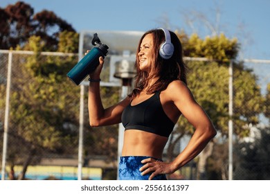 Beautiful woman in headphones drinking water after playing basketball - Powered by Shutterstock