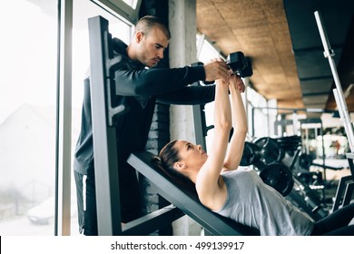 Beautiful Woman Helped By Trainer In Gym