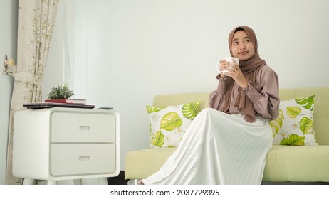 beautiful woman in hijab sitting relaxed enjoying a drink at home - Powered by Shutterstock