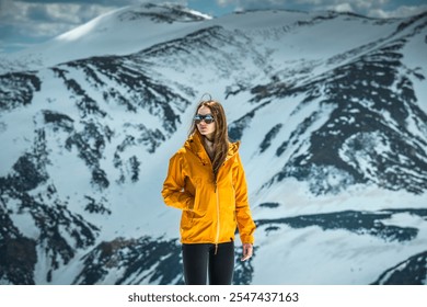 Beautiful Woman Hiking in Mountains Contemplating View of Winter Mountains. Portrait of female in orange windproof jacket feeling freedom getting to the top of the snowy mountain peak admiring scenic  - Powered by Shutterstock