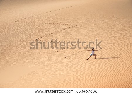 Beautiful woman hiking on giant sand dunes while making a zig zag pattern. Liwa desert, UAE.