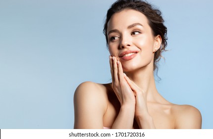 Beautiful Woman Hold Folded Palm Near Face. Millennial Lady Enjoying Soft Smooth Skin On Hand Face. Smiling Model Looking Aside. Studio Portrait On Blue