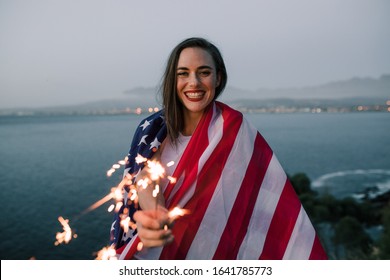 Beautiful woman holding American flag celebrating holding sparkles - Powered by Shutterstock