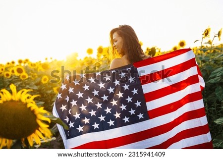 Beautiful woman holding an American flag in a sunflower field at sunset. Patriotic holiday. Independence Day, July 4th.