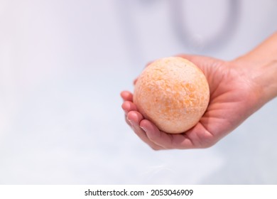 Beautiful Woman Holding An Aromatic Orange Bath Bomb On Her Hands Before Put It Into The Bathtub. Wellness And Hydro Therapy Relaxation Concept.