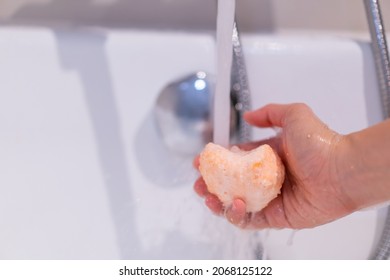 Beautiful Woman Holding An Aromatic Orange Bath Bomb On Her Hands Before Put It Into The Bathtub. Wellness And Hydro Therapy Relaxation Concept.