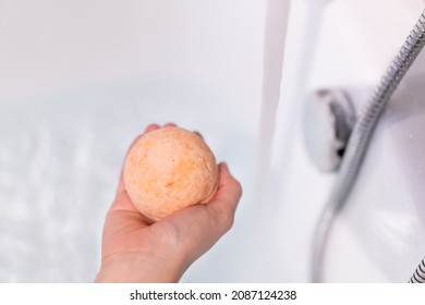 Beautiful Woman Holding An Aromatic Orange Bath Bomb On Her Hands Before Put It Into The Bathtub. Wellness And Hydro Therapy Relaxation Concept.