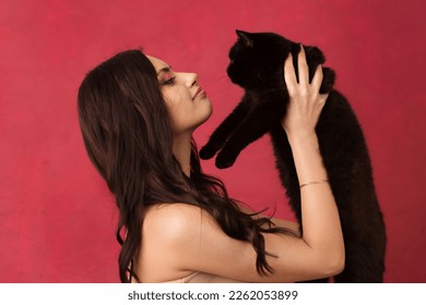 Beautiful woman holding a black cat on a pink background. - Shutterstock ID 2262053899