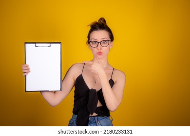 Beautiful Woman Holding A Flyer.Studio Shoot.Young Woman In Front Of Yellow Backdrop.Your Message Is Here.