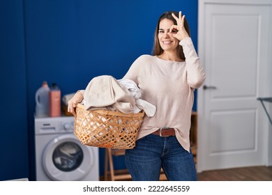 Beautiful Woman Holding Laundry Basket Smiling Happy Doing Ok Sign With Hand On Eye Looking Through Fingers 