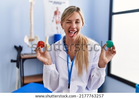 Beautiful woman holding strength ball for hand rehabilitation sticking tongue out happy with funny expression. 