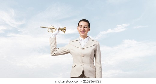 Beautiful woman holding trumpet brass near ear and listening. Young businesslady in white business suit and gloves posing with music instrument on blue sky background. Business concept with musician