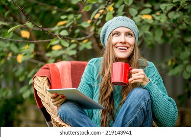 Beautiful Woman With Hot Tea Using Tablet Computer In Autumn Garden Looking Up. Copy Space