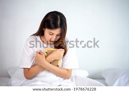A beautiful woman hugged a photo with a sad feeling and crying in the bedroom in a sad mood.