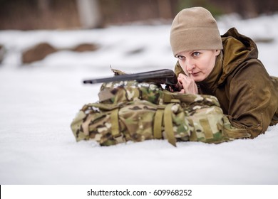 beautiful woman hunter with a rifle lying in the snow forest. Bushcraft, hunting and people concept