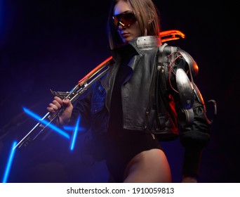 Beautiful woman with implant wearing black clothing and sunglasses in dark background. Female mercenary holding a glowing sword on her shoulder.