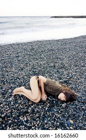 Beautiful woman laying on the beach with sad gesture. Long exposed waves.