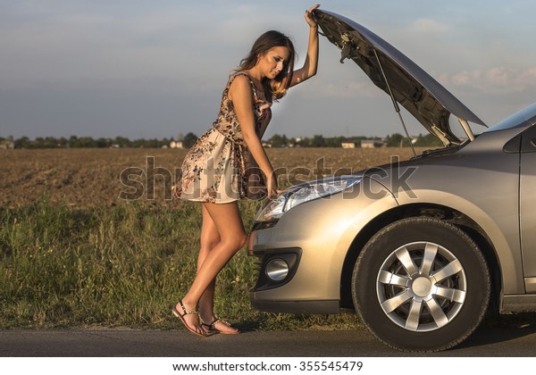 Beautiful woman leaning over looking into the\
engine compartment of a broken down\
car.