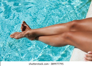 Beautiful woman lgs in swimming pool. Tanned feet with pedicure in the pool water.