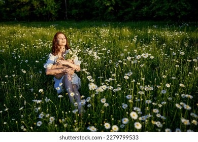 a beautiful woman in a light dress sits in a field of daisies with a wicker basket in her hands in the rays of the setting sun - Shutterstock ID 2279799533