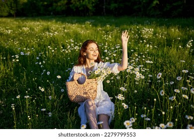 a beautiful woman in a light dress sits in a field of daisies with her hands raised above her head in the rays of the setting sun - Shutterstock ID 2279799553