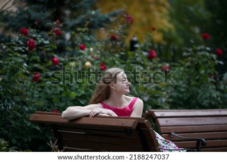Beautiful woman with long blond hair. A woman walks in a rose garden. Beautiful rose garden. Dress with floral print.
