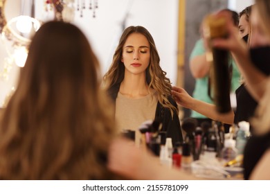 Beautiful Woman With Long Blonde Hair Sitting In Front Of A Mirror While A Hairdresser Styling Her Hair