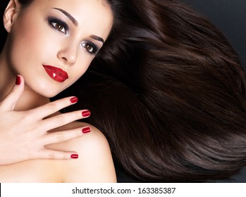 Beautiful Woman With Long Brown Straight Hairs And Red Nails Lying On The Dark Background
