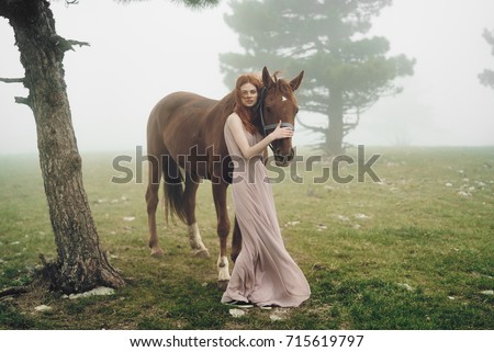 beautiful woman in a long dress with a horse in foggy weather outdoors in the forest, clean air                               