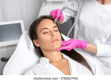 Beautiful woman with long hair, with clean fresh skin.Cosmetologist makes  procedure microdermabrasion on the face. Women's cosmetology in the beauty salon.