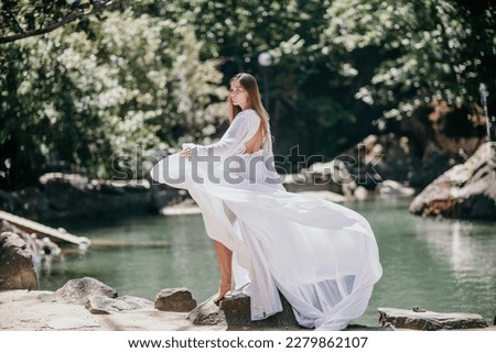 a beautiful woman in a long white dress looks into the distance at a beautiful lake with swans rear view