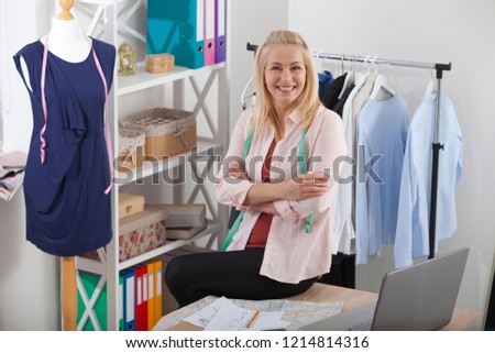 Beautiful woman looking at camera, standing near the table in the workshop with clothes.