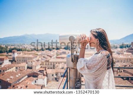 Beautiful woman looking at coin operated binocular on terrace at small town in Tuscany, Italy