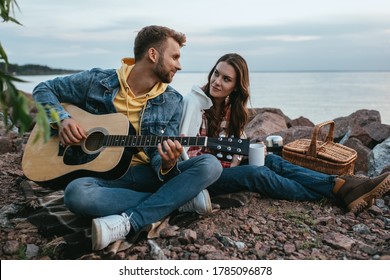 Beautiful Woman Looking At Handsome Boyfriend Playing Acoustic Guitar Outside