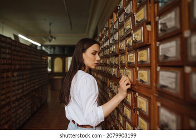 Beautiful woman looking for information in the old library archive, opens a box with a database of books.