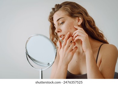 A beautiful woman looking in the mirror, touching her face with her hand, examines acne, pigmentation. The concept of rosacea and couperose. Cosmetic care. Allergic reaction.